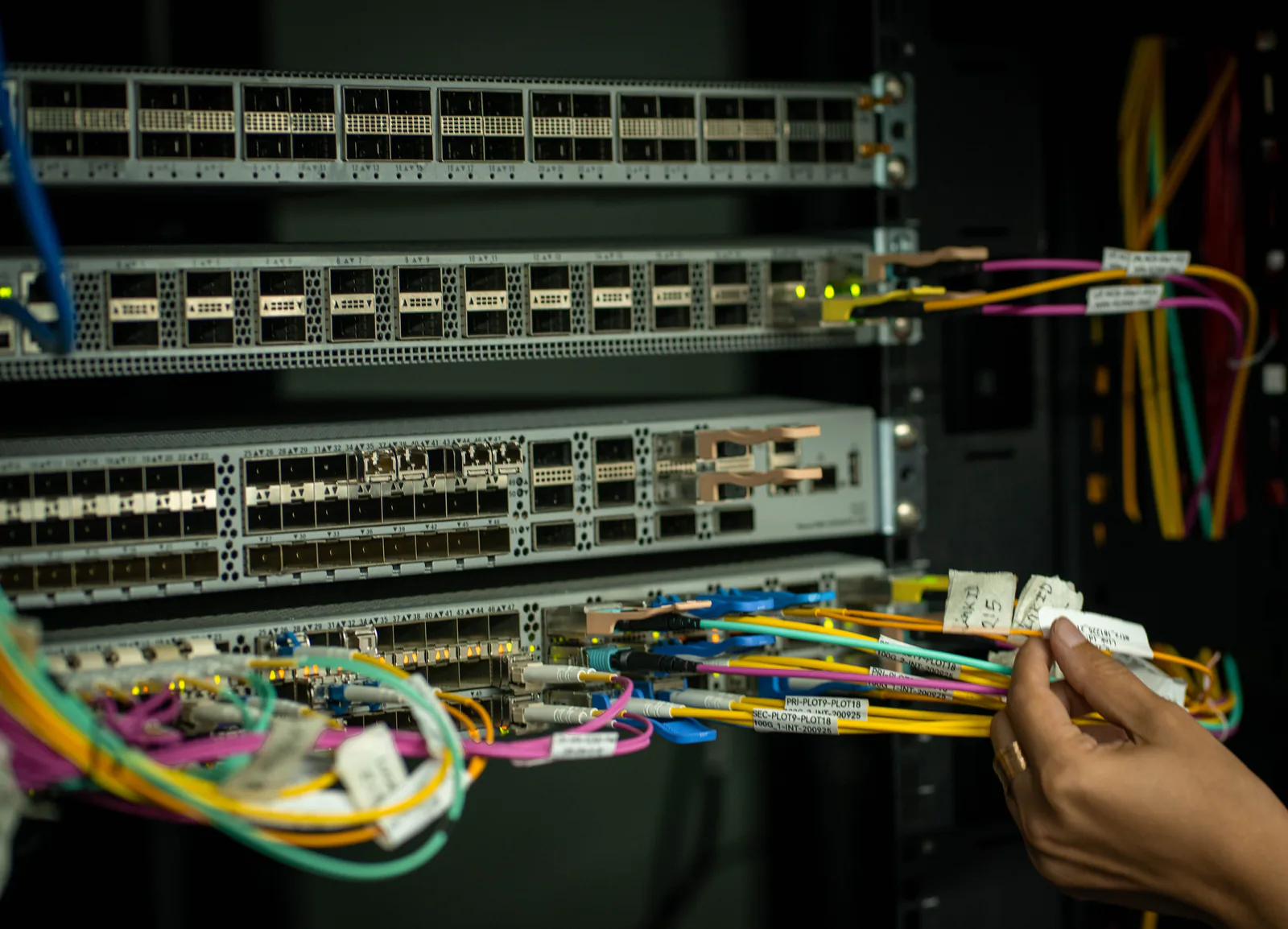 A technician's hand routing labelled fibre patch cords into a network switch